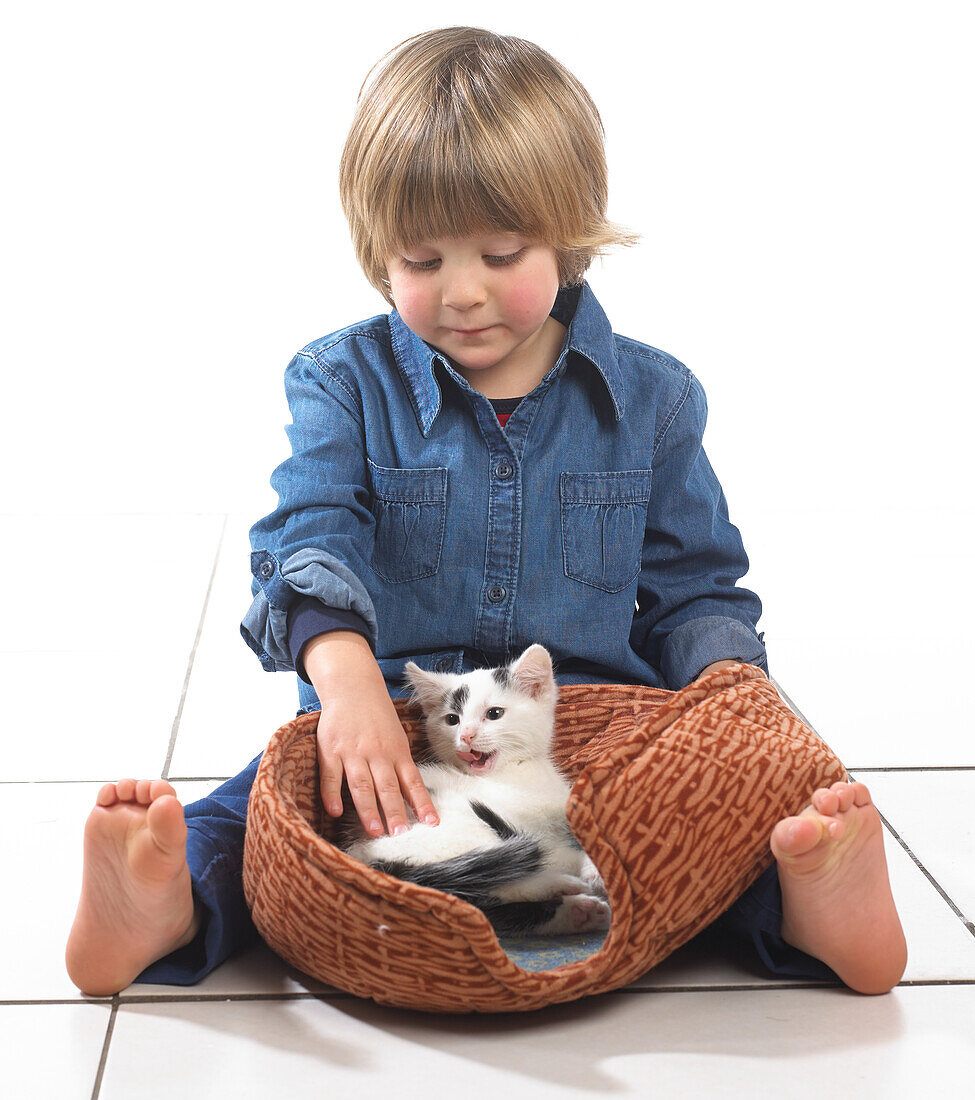Boy sitting with kitten in pet basket between his legs