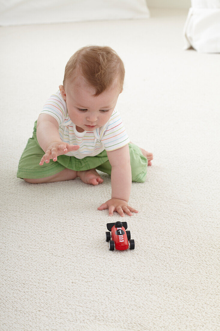 Baby boy sitting on carpet reaching for toy racing car