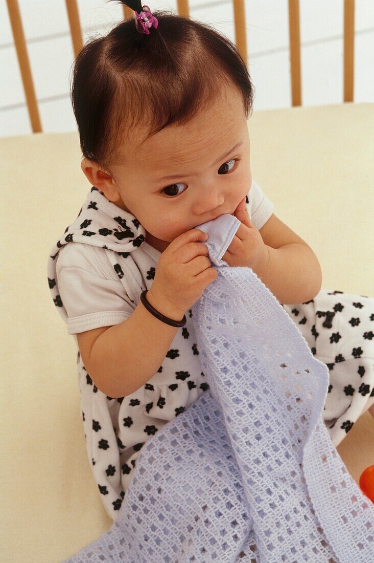 Baby girl sat chewing her blanket