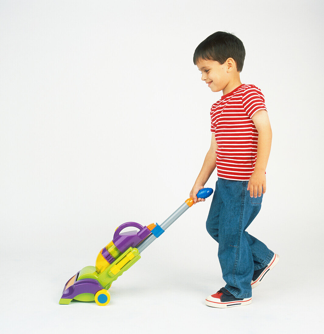 Boy pushing toy vacuum cleaner by handle