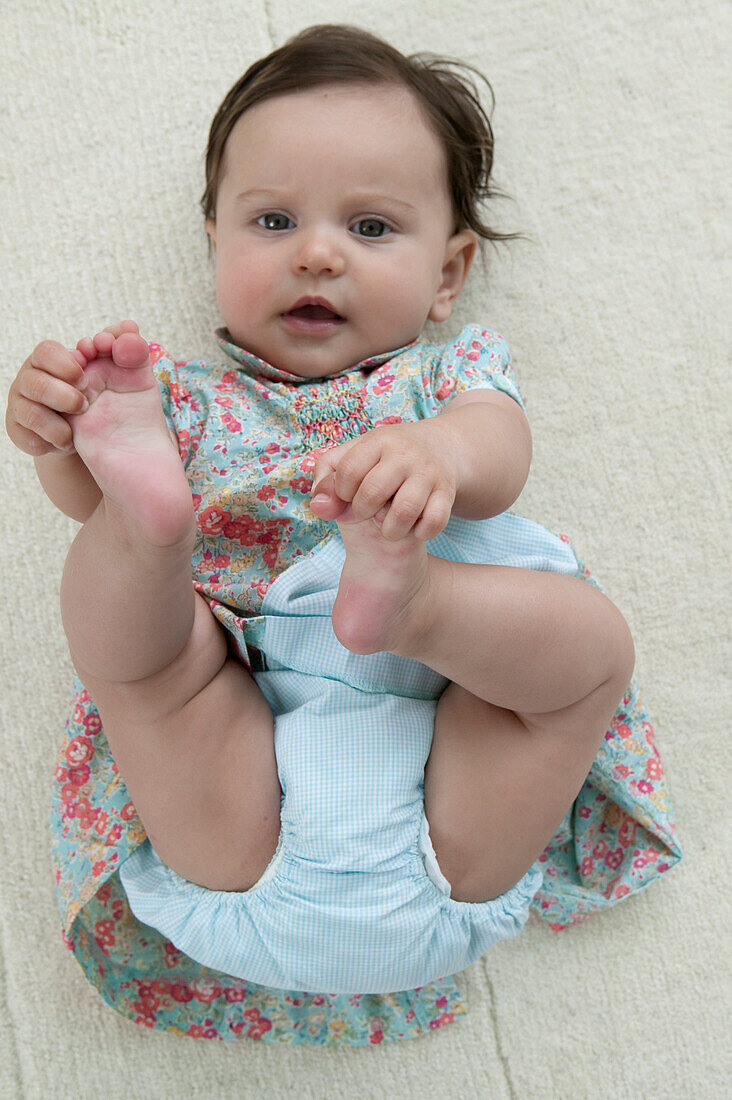 Baby girl lying on back holding feet