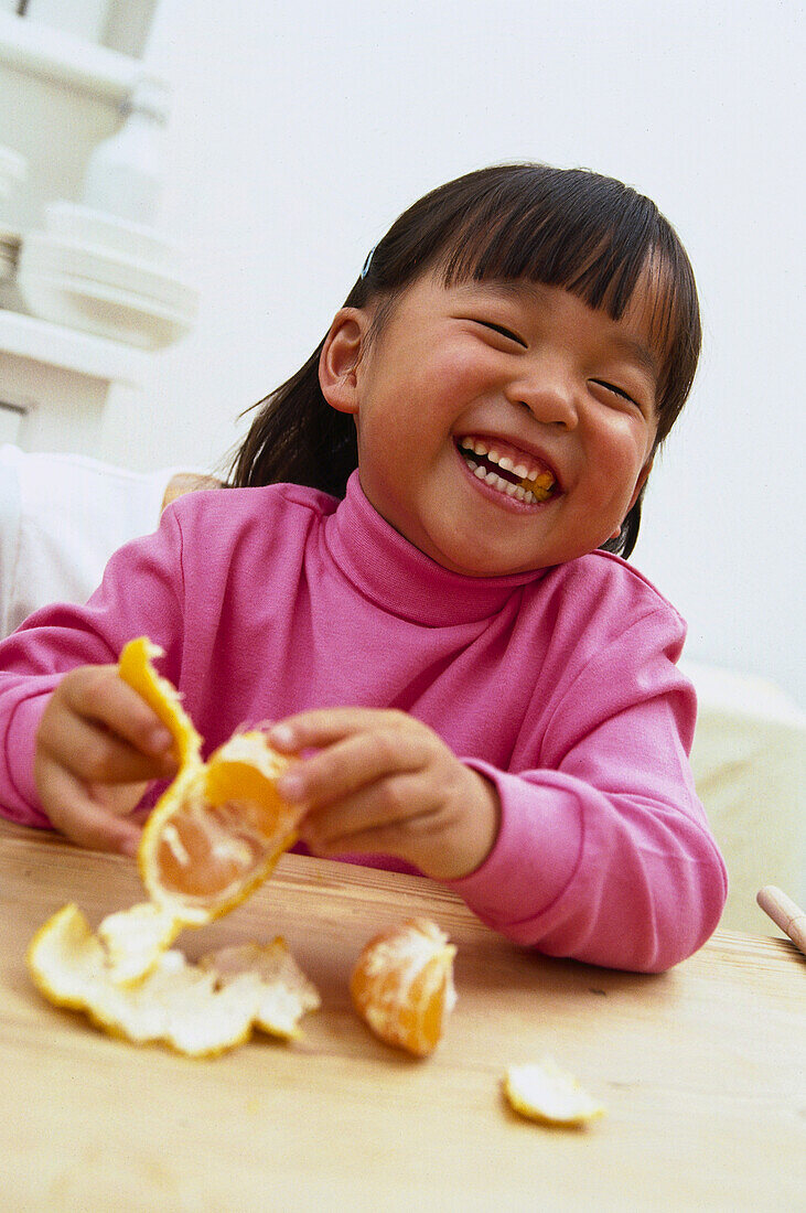 Young girl laughing while peeling a satsuma