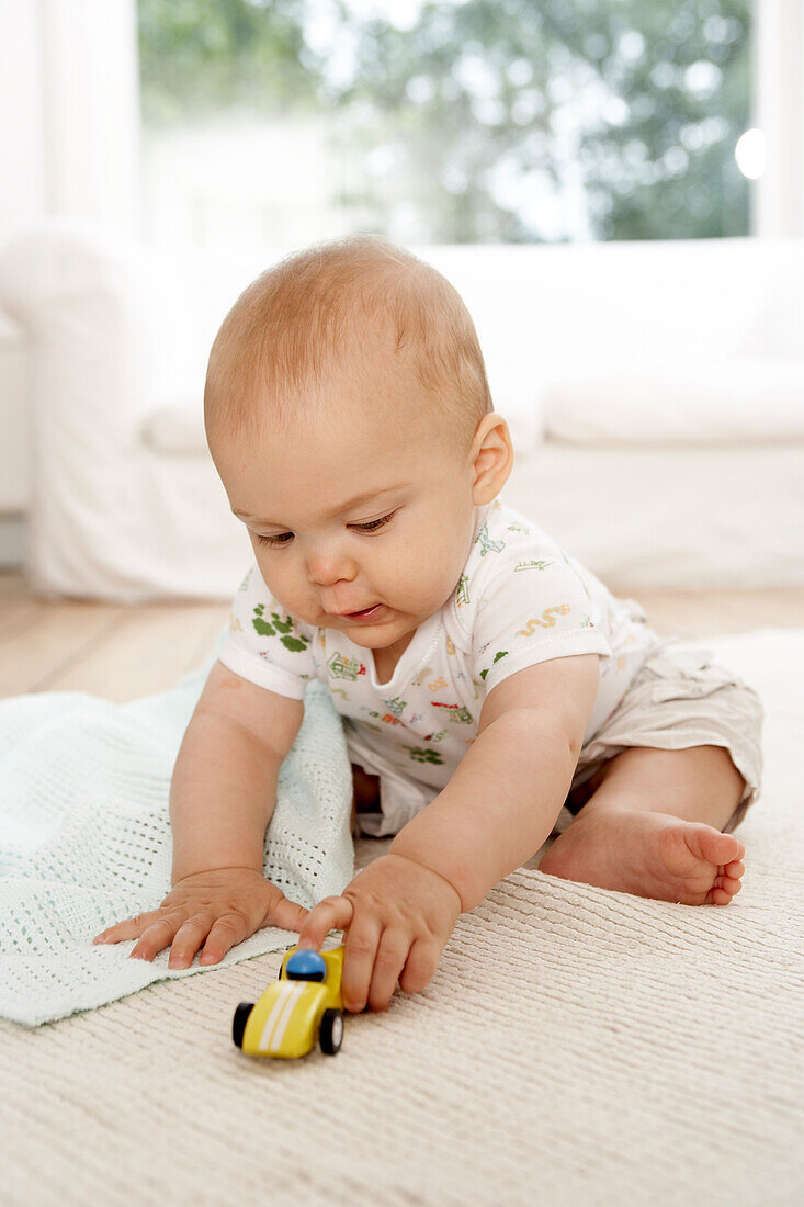Baby boy playing with small toy car on mat