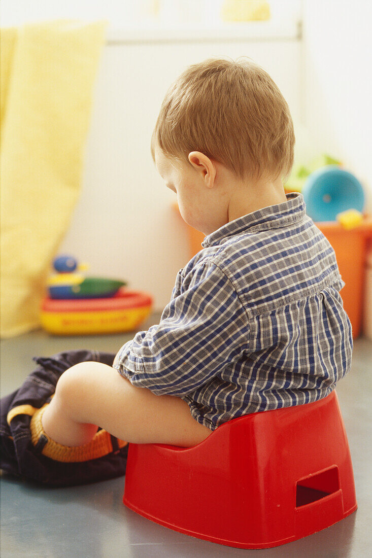 Boy toddler sitting on plastic potty with trousers down