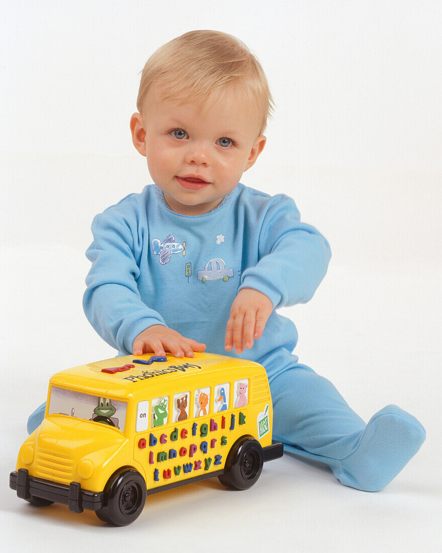 Baby boy playing with yellow plastic toy bus