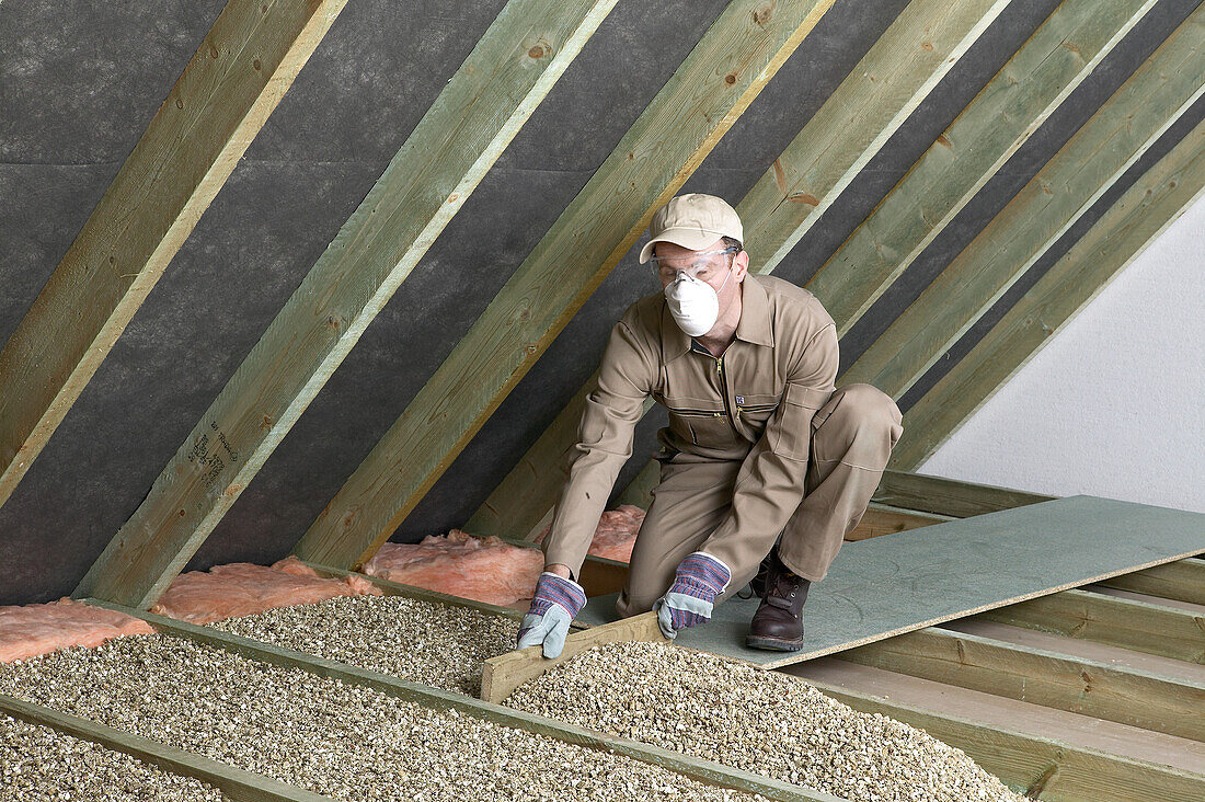 Man levelling loose-fill insulation between ceiling joists