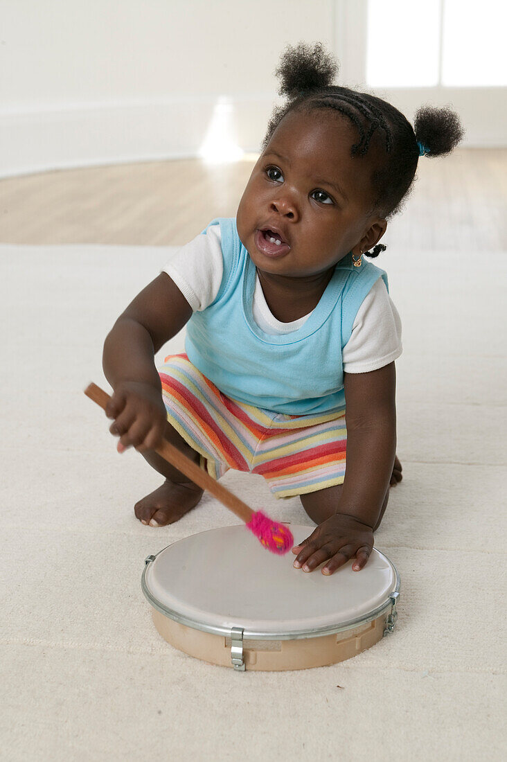 Baby girl playing with beater and tambourine