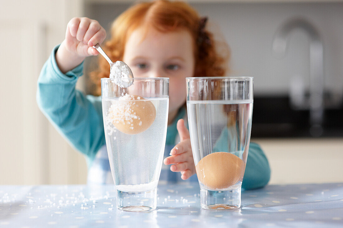 Eggs in glass and girl pouring salt in glass of water