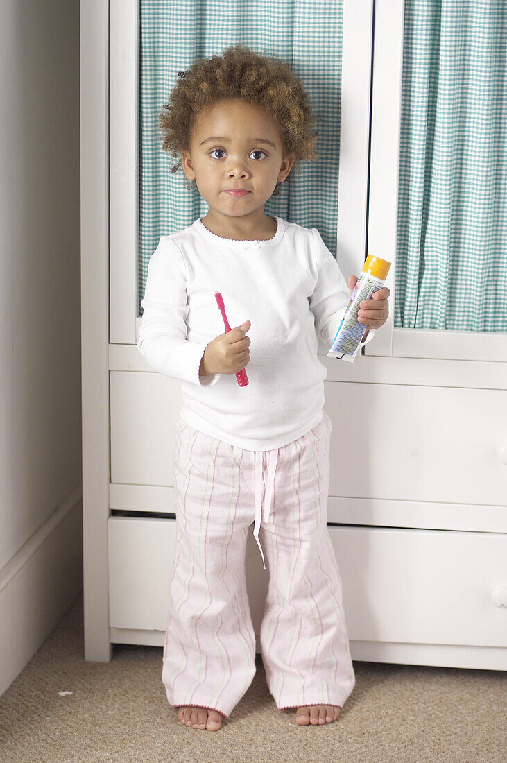 Toddler holding red toothbrush and tube of toothpaste