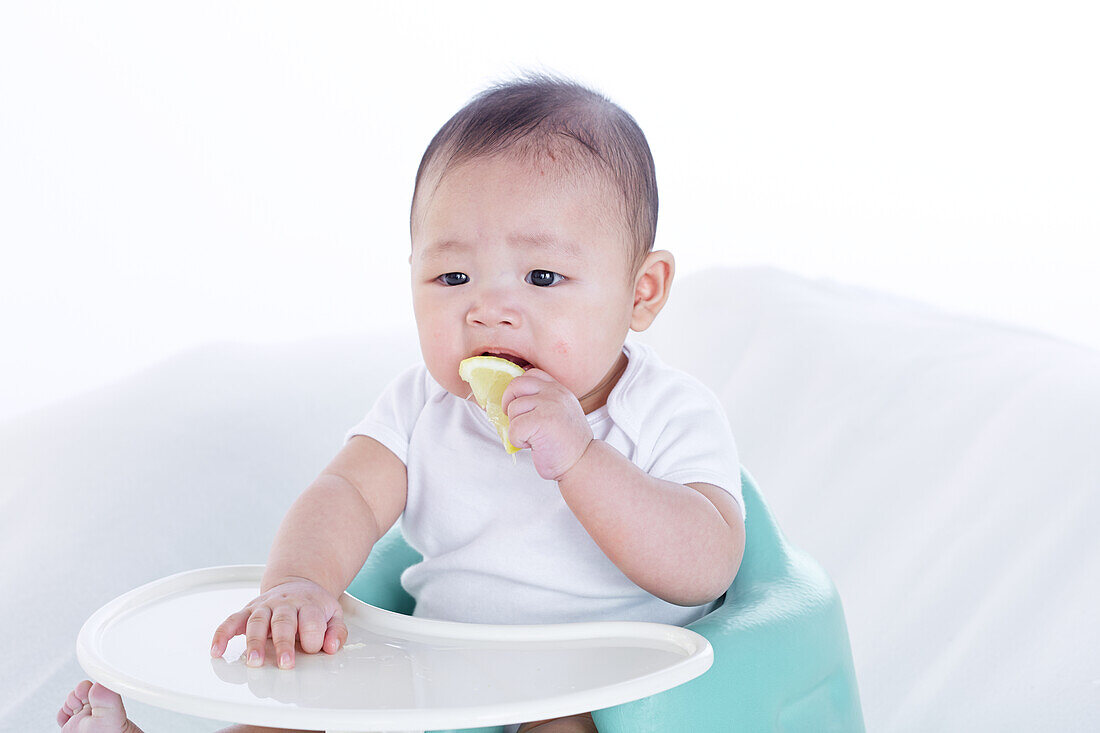 Baby boy sitting in high chair tasting lemon