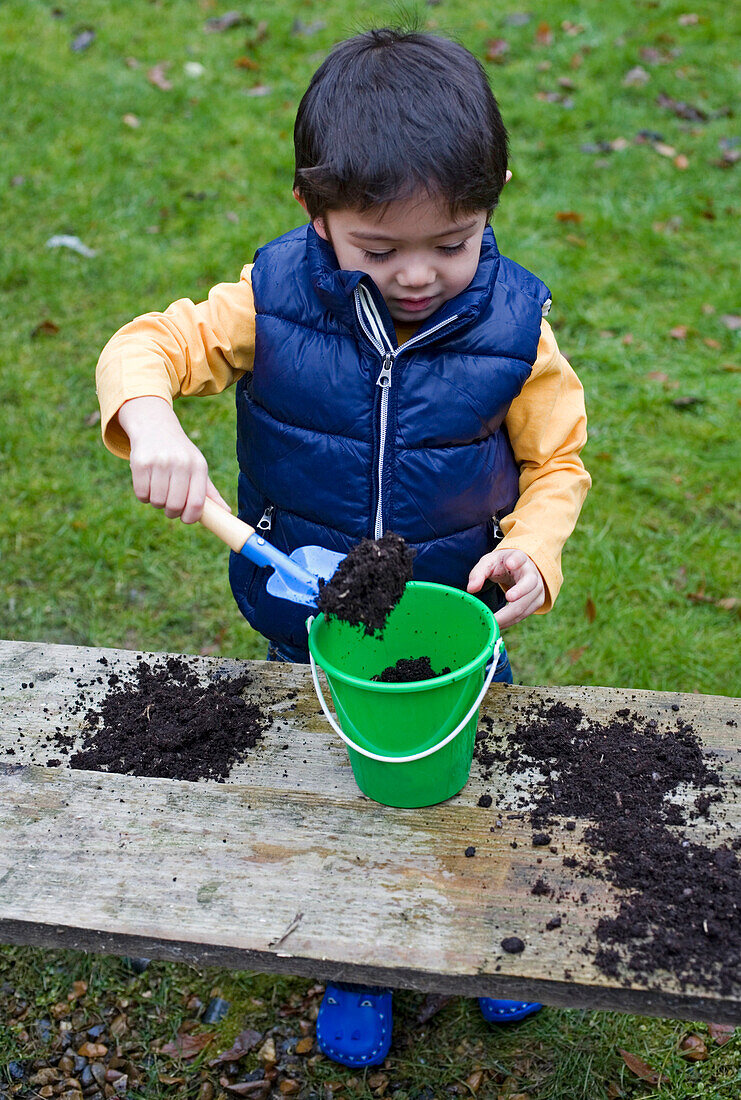 Boy holding trowel filled with compost above plastic bucket