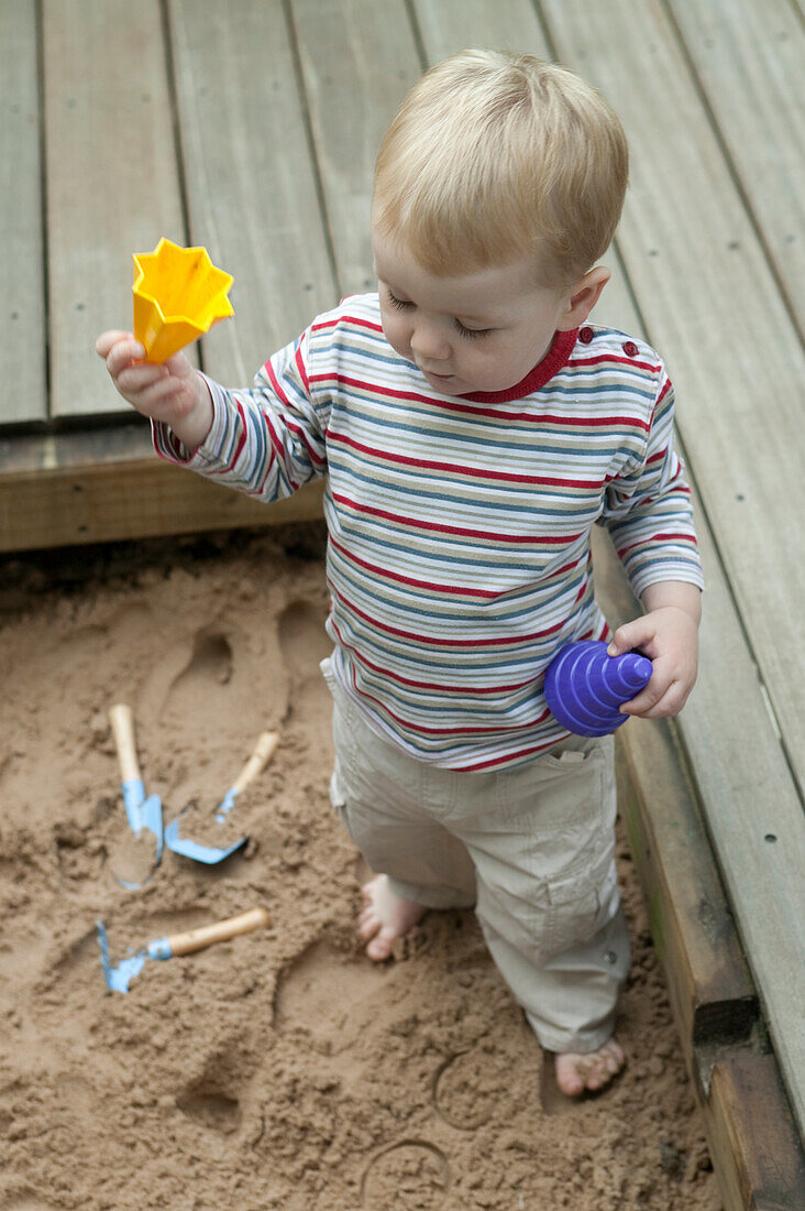 Baby boy playing with sand and plastic toys in sandpit