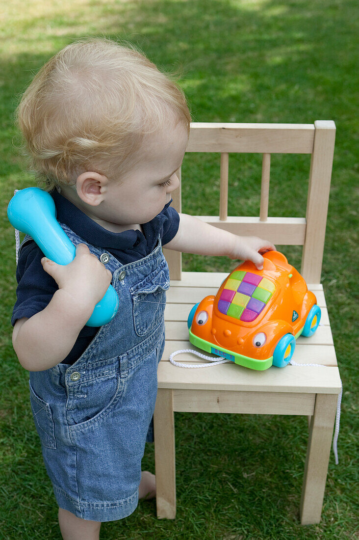 Toddler playing with toy telephone on chair in a garden