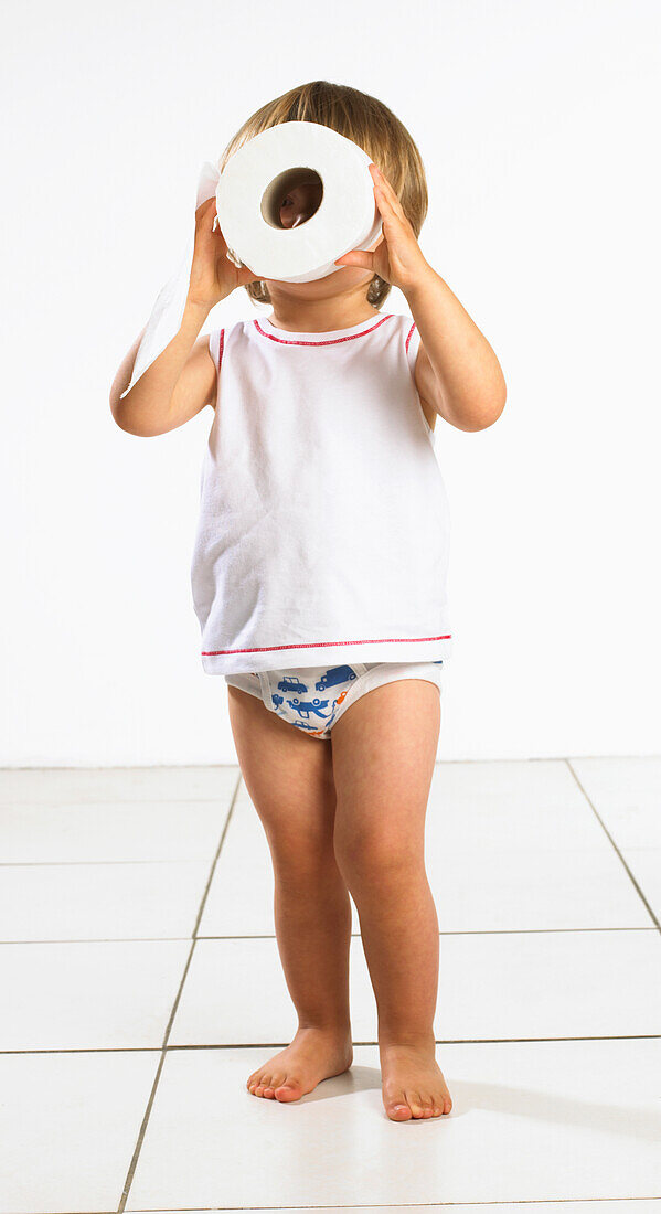 Toddler boy in underwear looking through toilet roll