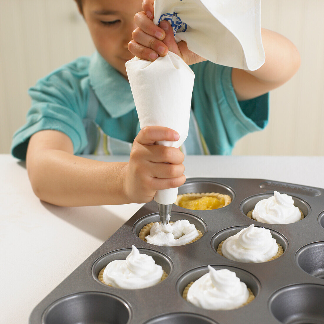 Boy piping meringue mixture onto apple tarts