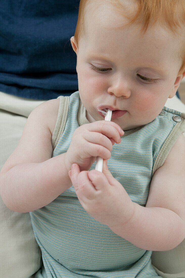 Baby boy in man's lap holding toothbrush in his mouth