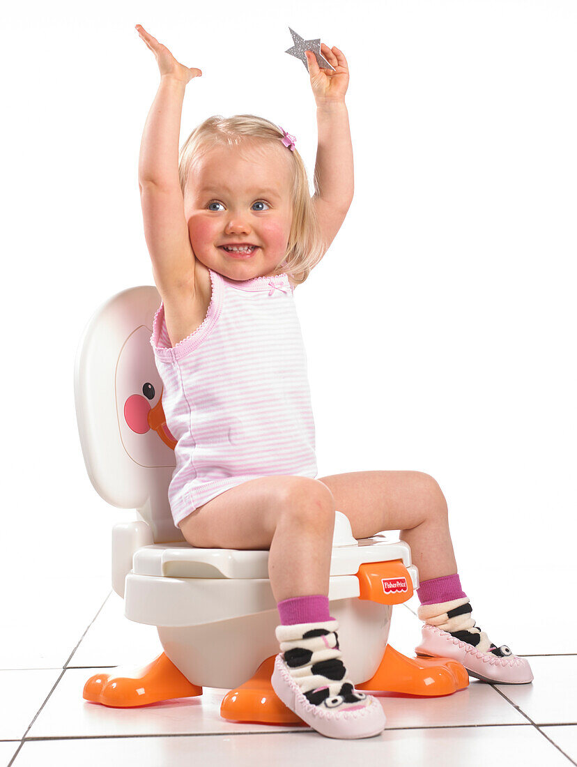 Girl sitting on white potty with arms in the air