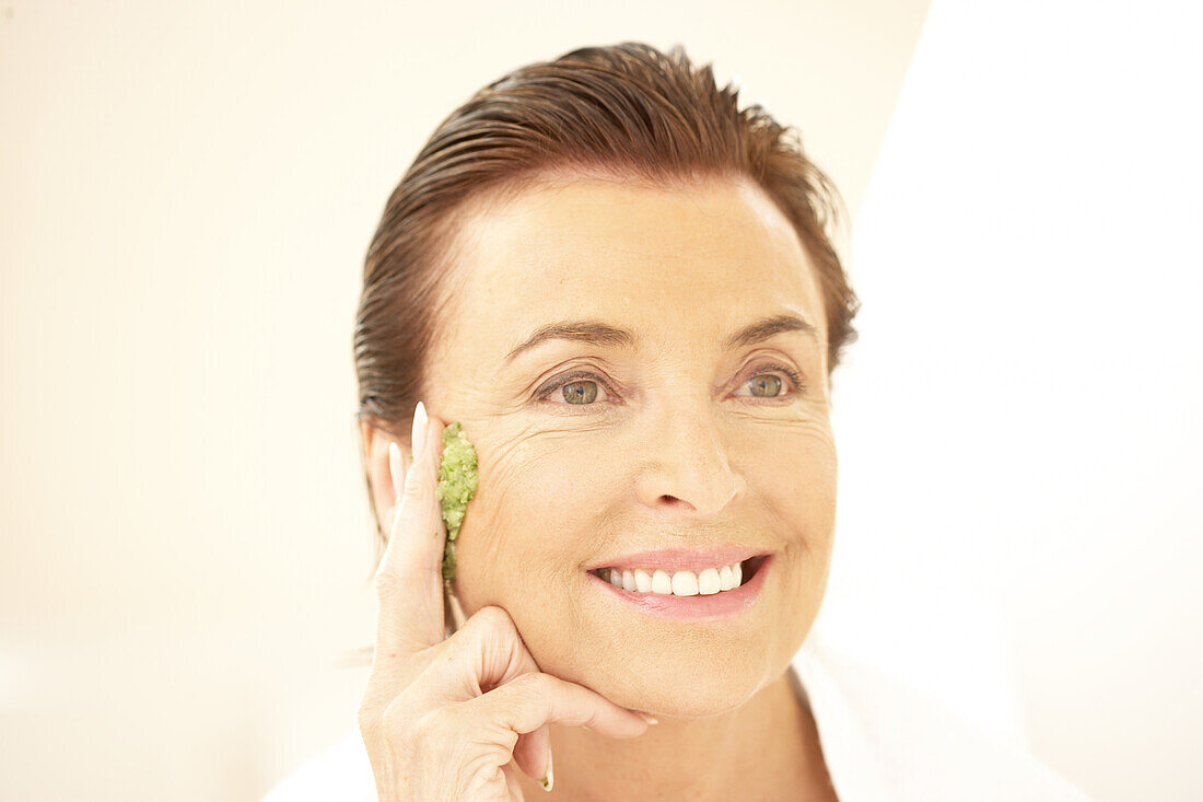 Smiling woman applying green face mask