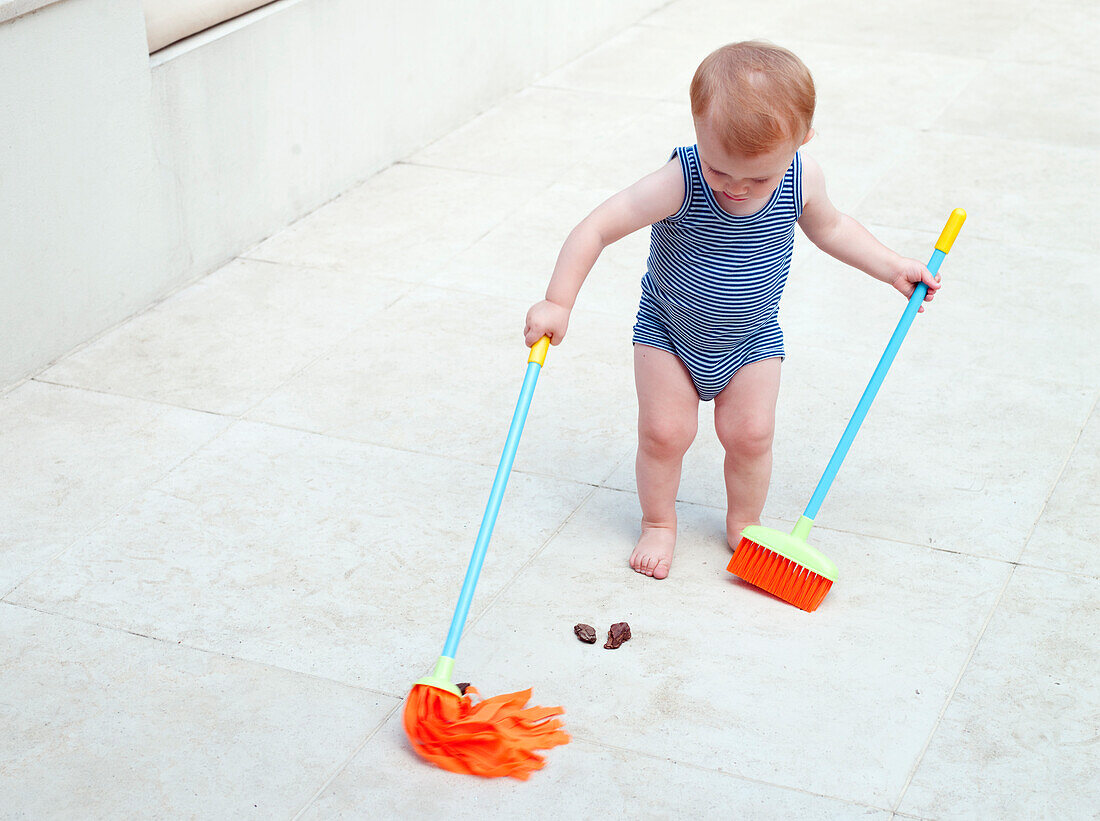 Baby girl holding a mop and a dustpan with long handle