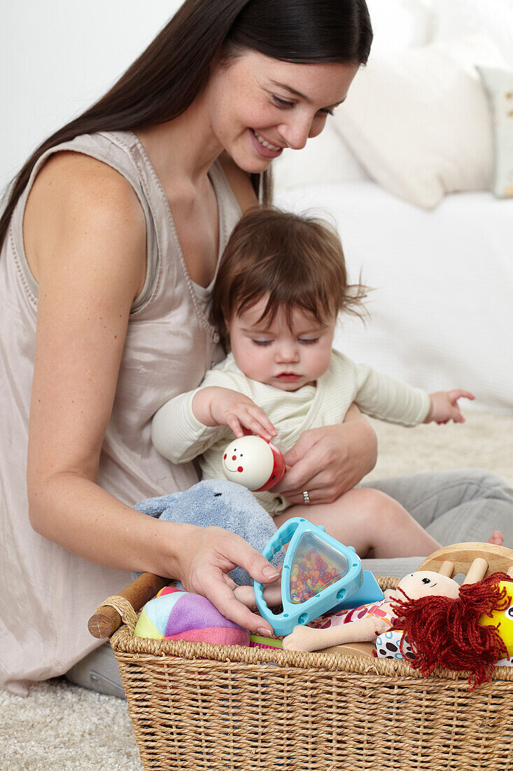 Mother with baby girl on her lap playing with basket of toys