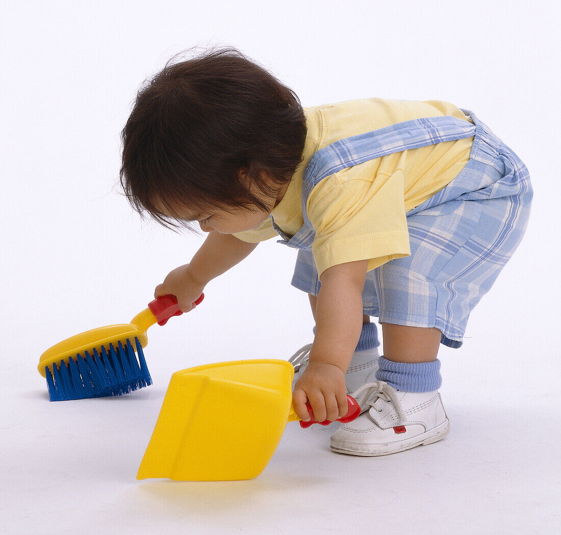 Toddler bending over to sweep floor with dustpan and brush