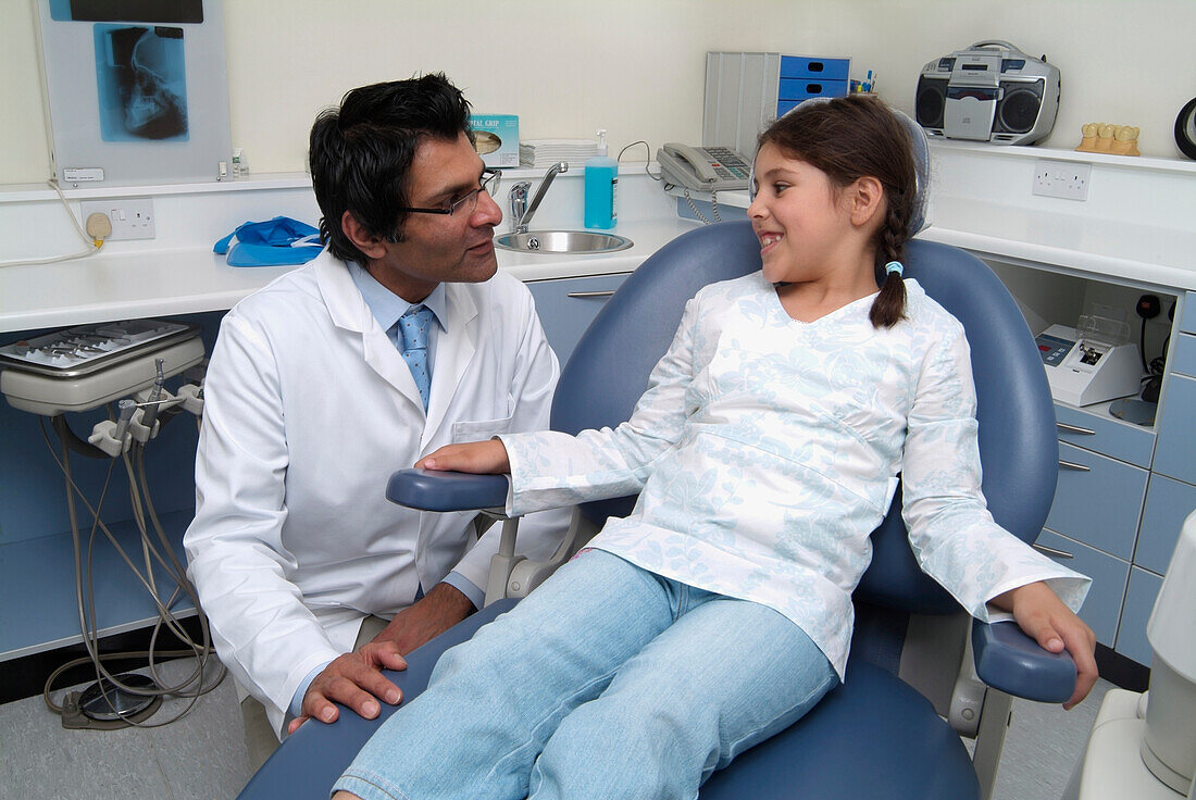 Dentist crouching beside girl in dentist's chair