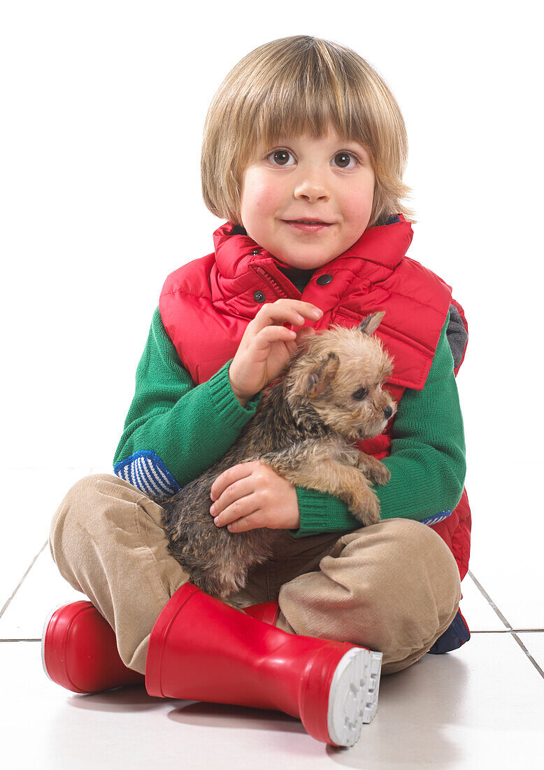 Boy wearing outdoor clothing sitting holding a puppy