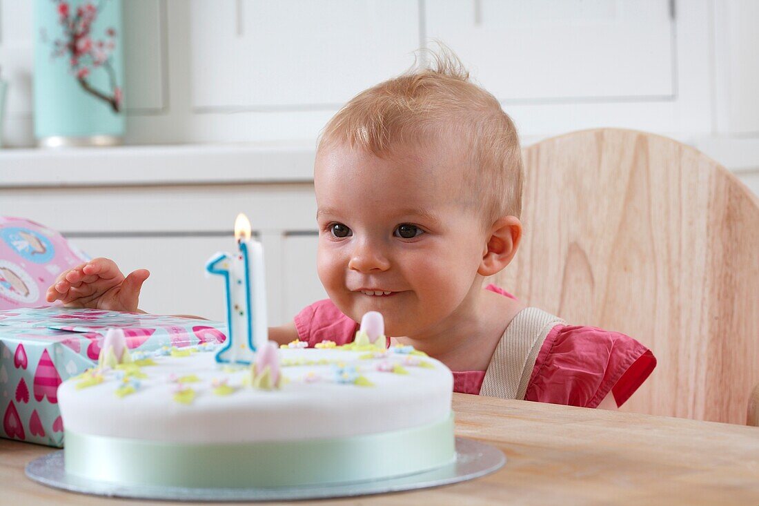 Baby girl sitting at table looking at 1st birthday cake