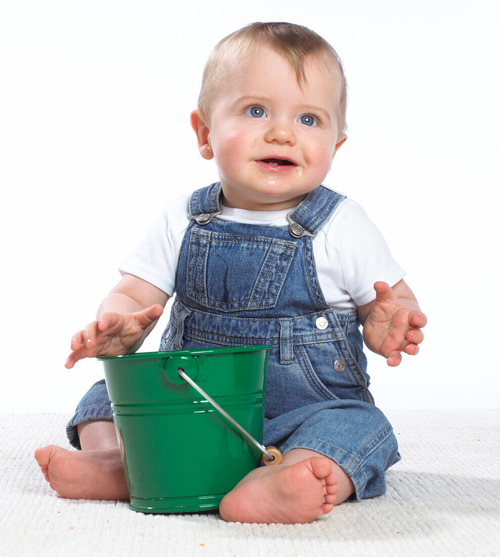 Baby boy sitting on floor with green bucket between legs