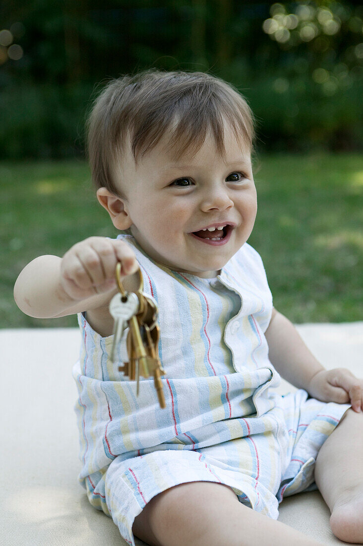 Baby boy sitting on blanket in garden holding set of keys