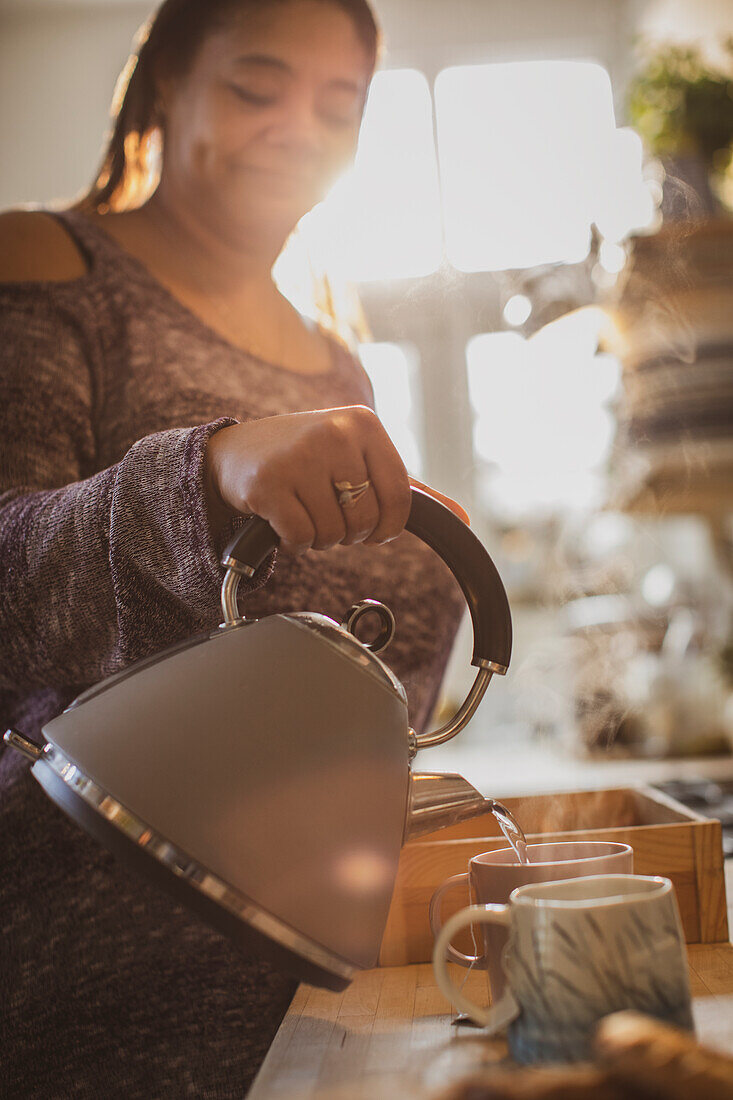 Woman with teapot pouring hot tea into mugs