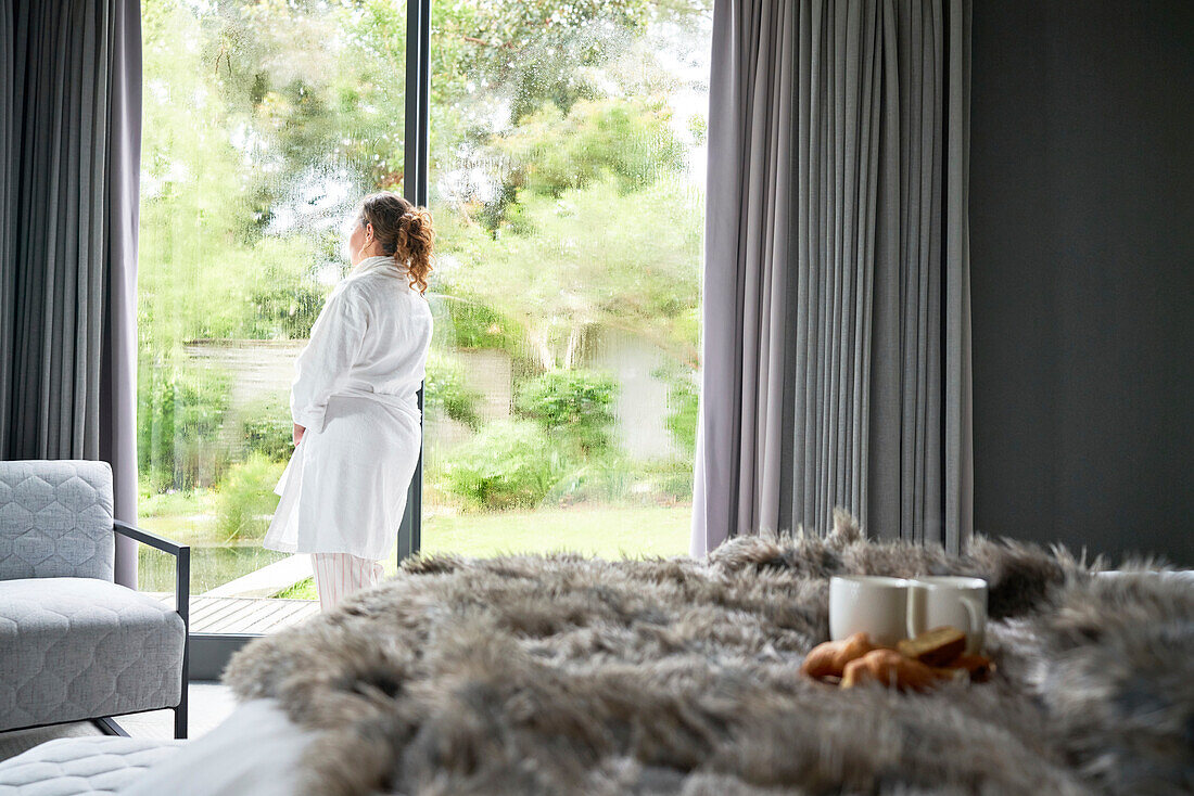 Woman in bathrobe standing at bedroom window