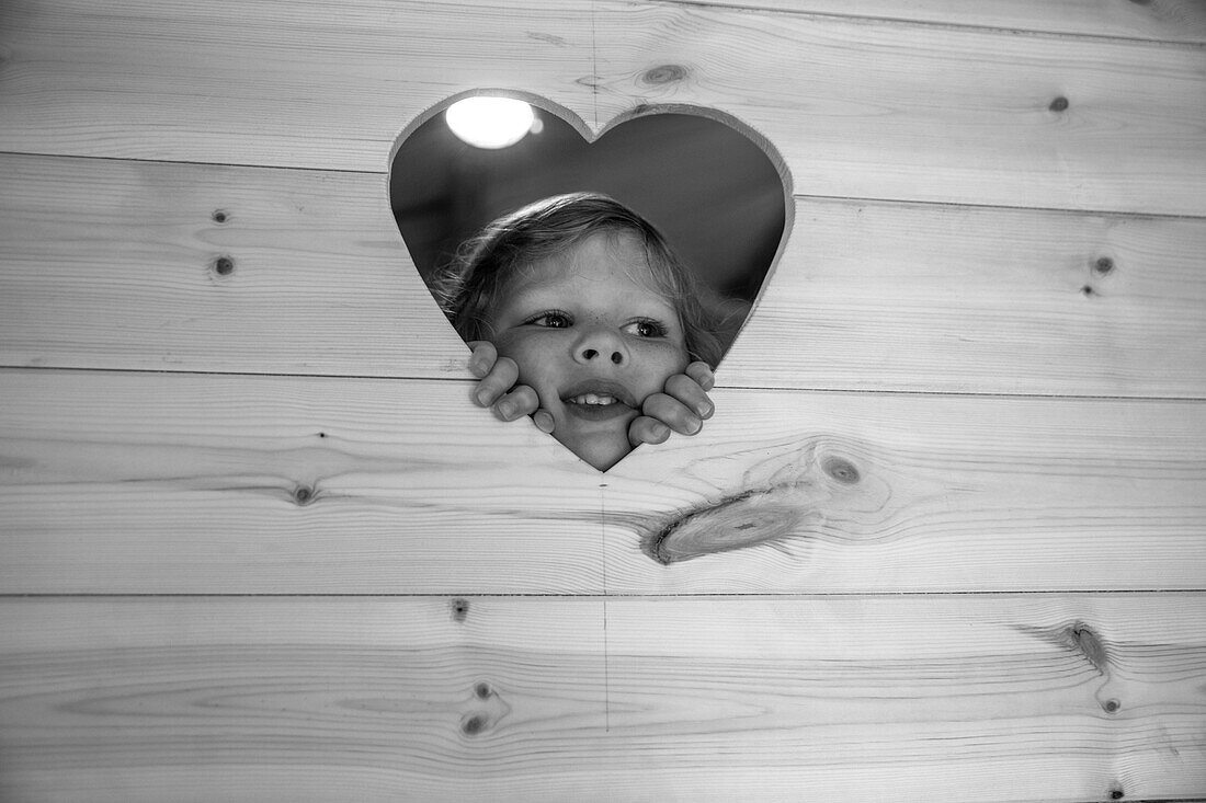 Girl peering through heart shape in wood