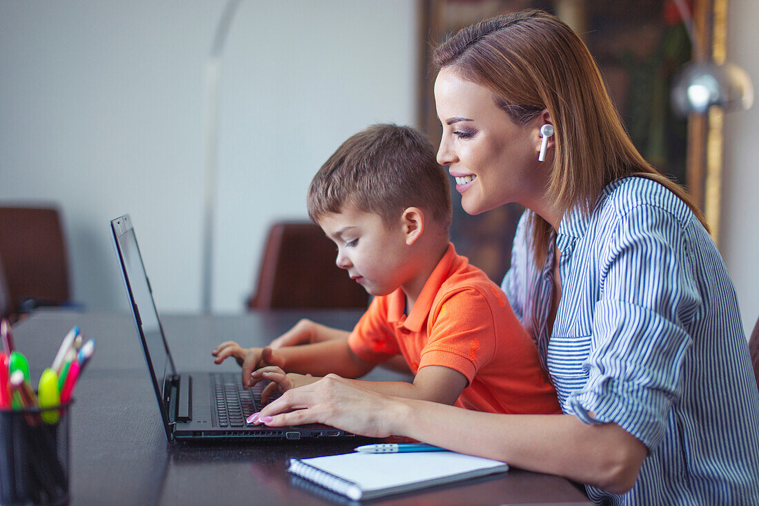 Businesswoman teaching typing to son on laptop at home