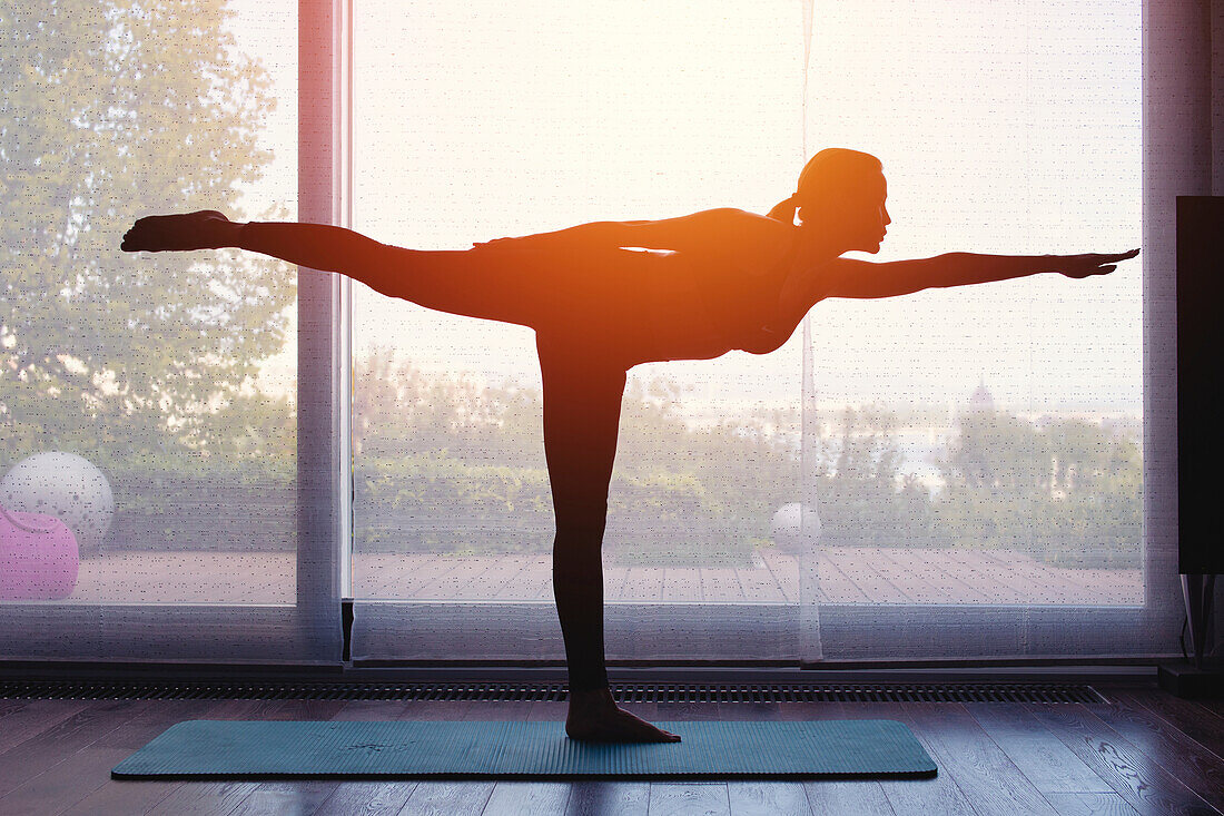 Silhouette of woman doing yoga at home at sunset
