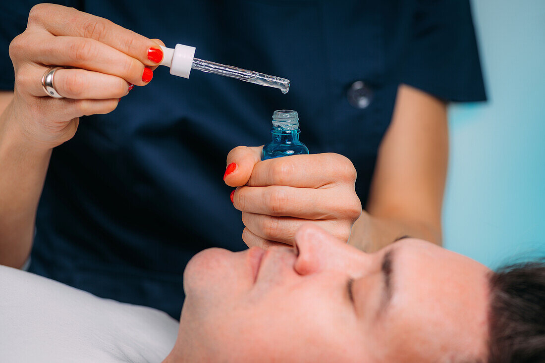 Cosmetician applying hyaluronic acid serum to man's face