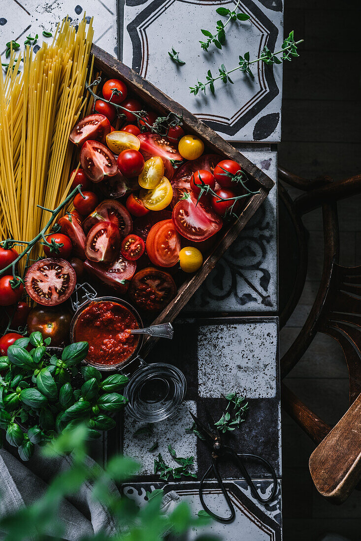 Bunte Tomaten, Pesto Rosso, Spaghetti und Basilikum in rustikaler Holzkiste