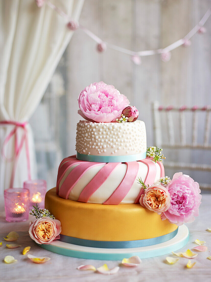 Wedding cake with orange iced layer, pink ribbon middle layer and the top layer with small bobbles of white icing