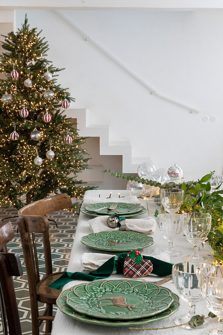 Dining table set for Christmas with green plates, decorated Christmas tree