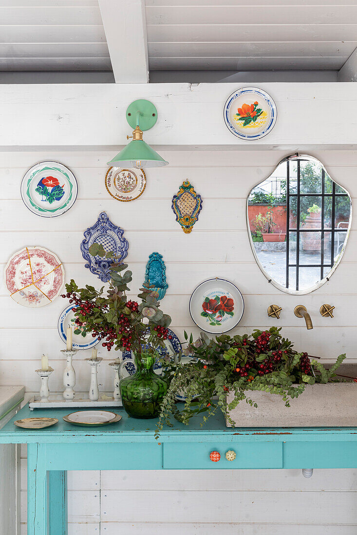 Wall decoration with colourful plates and mirror above blue console