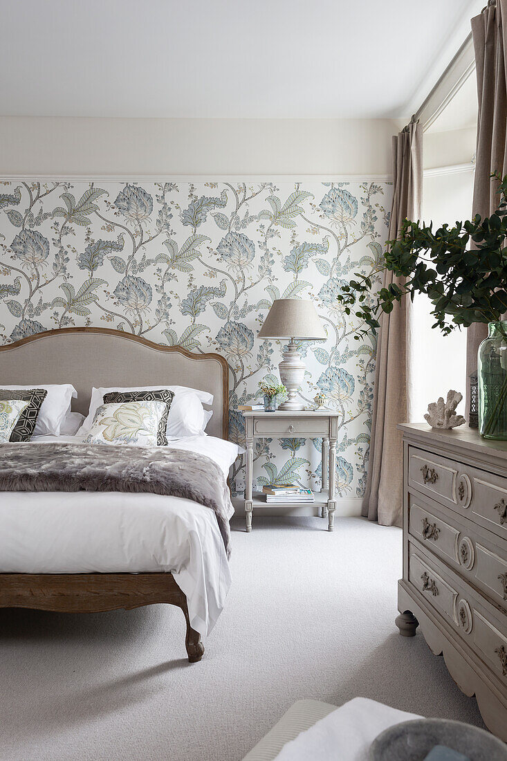 Double bed with bedside table in front of patterned wallpaper, chest of drawers in the foreground