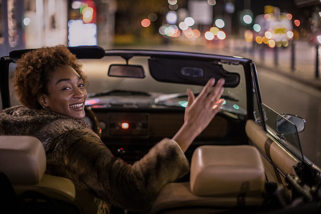 Carefree young woman driving convertible in city at night