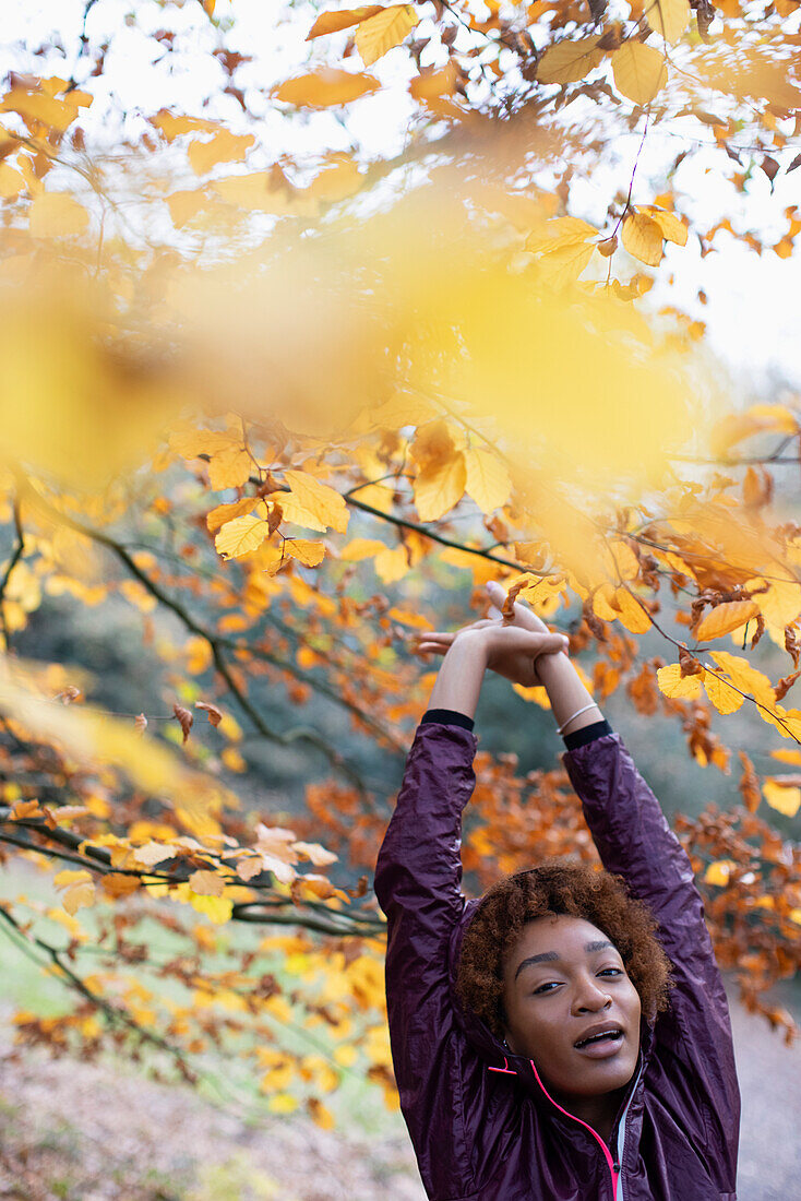 Young woman stretching below autumn tree