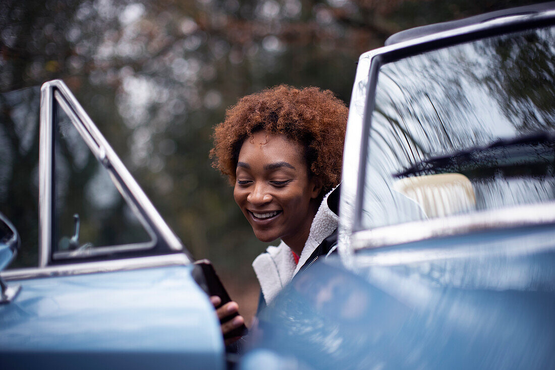 Happy young woman using smartphone at convertible