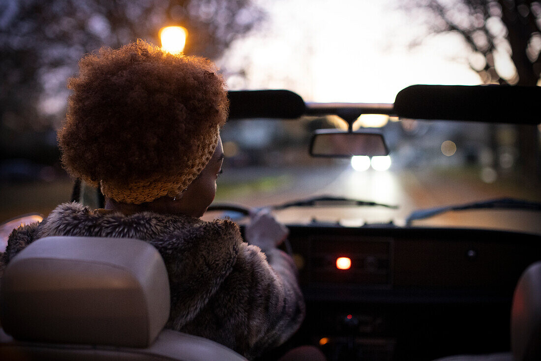 Young woman driving convertible on road at dusk