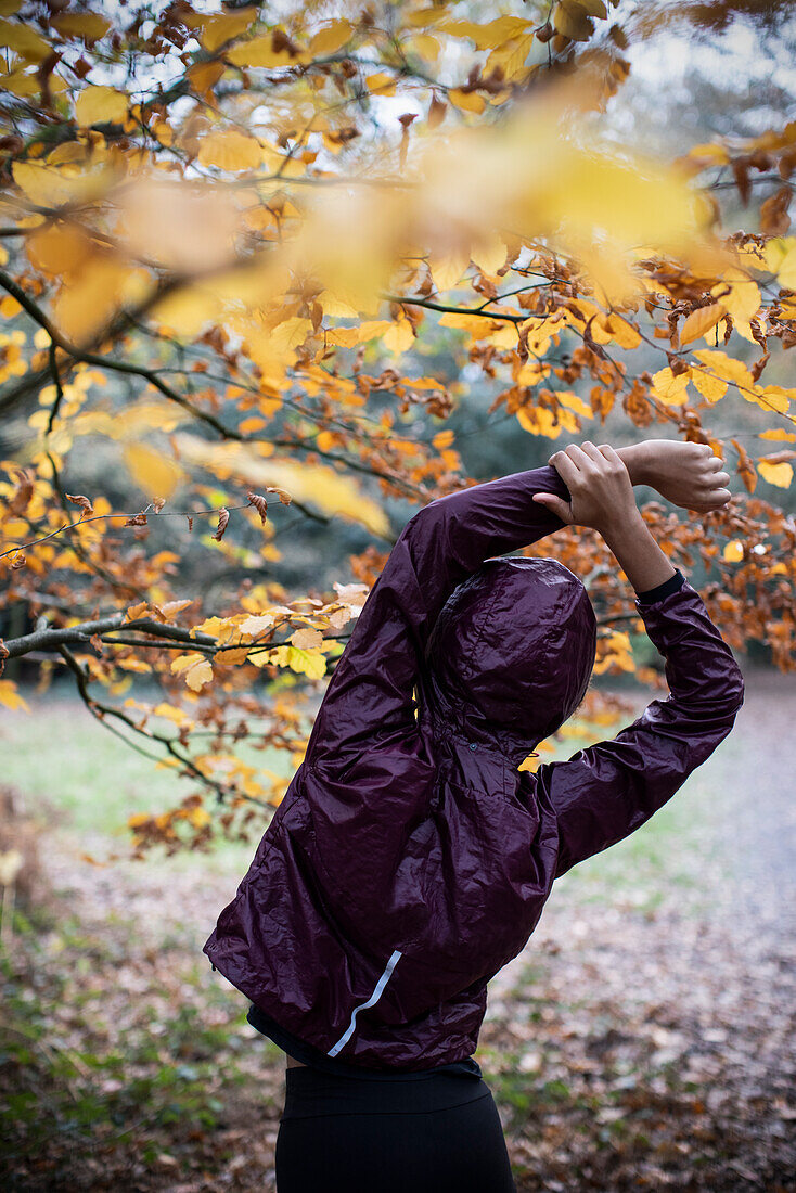 Young female runner stretching arms below autumn tree