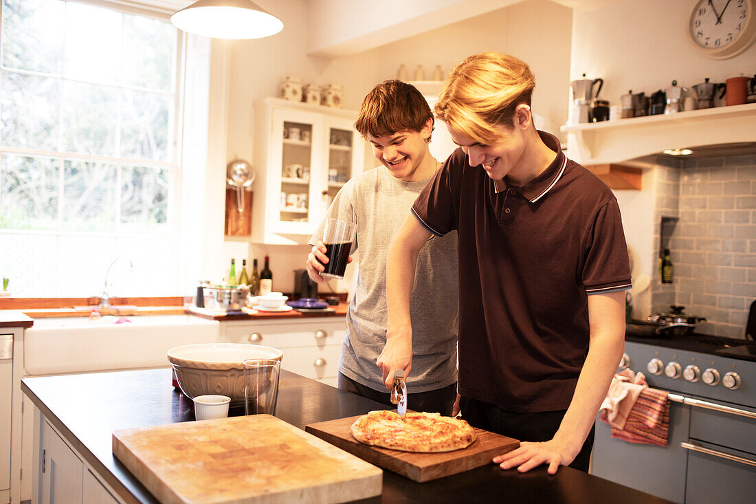 Happy teenage boys slicing pizza in kitchen