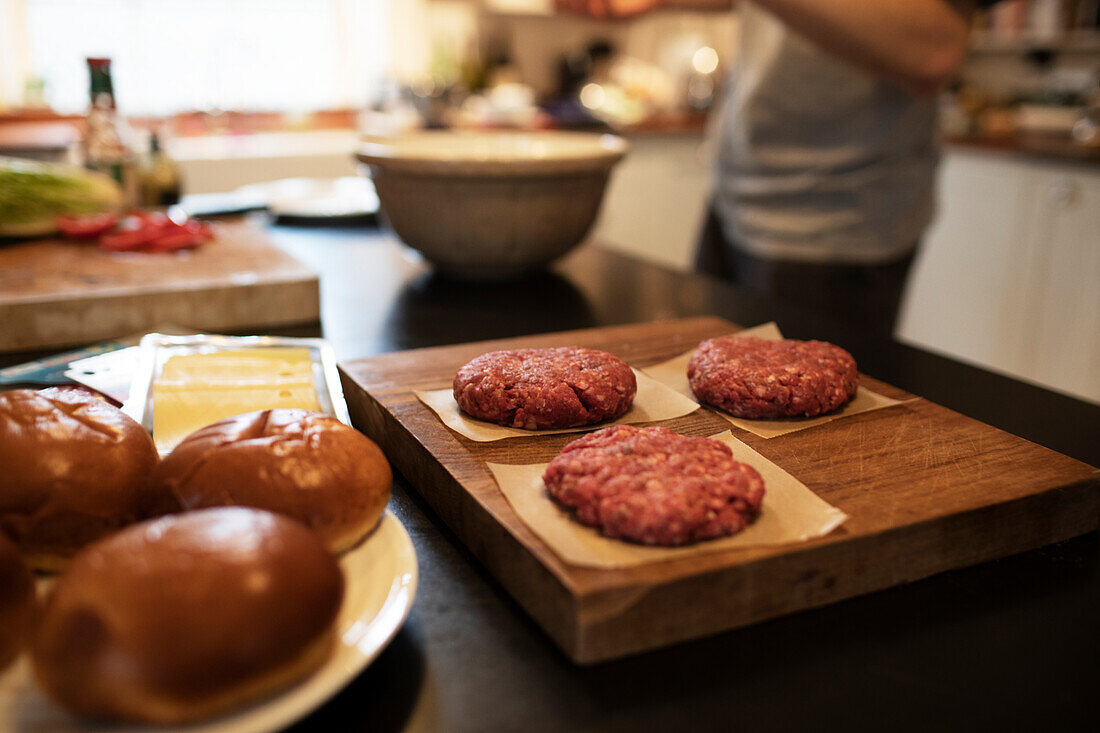 Fresh hamburger patties and buns on kitchen counter