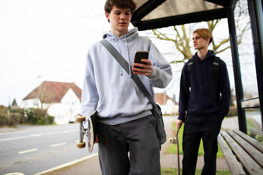 Teenage boys with skateboards and smartphone at bus stop