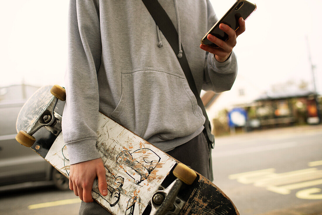 Teenage boy with skateboard and smartphone on street